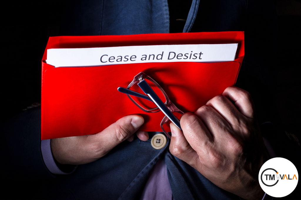 A person holding a red envelope labeled "Cease and Desist," along with a pair of glasses, against a dark background. The TM WALA logo is visible in the corner.