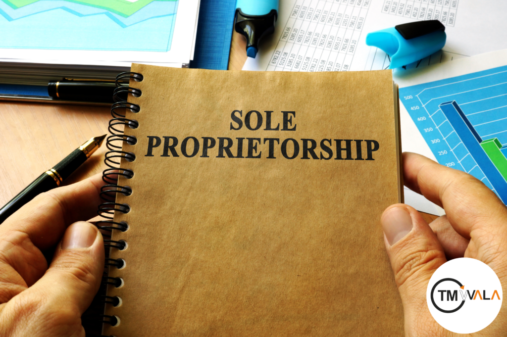 A business notebook with "SOLE PROPRIETORSHIP" written on the cover, held by a person, surrounded by financial documents, a pen, and a highlighter. Represents Sole Proprietorship Registration and business setup.